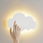 Sobre un fondo blanco, vemos un aplique en forma de nube blanca, encendido, y una mano de mujer sobre la nube.