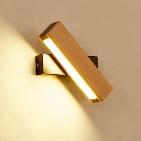 Aplique LED rectangular de madera sobre una base negra rectangular. El rectángulo de madera con la fuente de luz es triangular, mientras que la base negra es horizontal. La luz está encendida. El aplique cuelga de una pared beige.