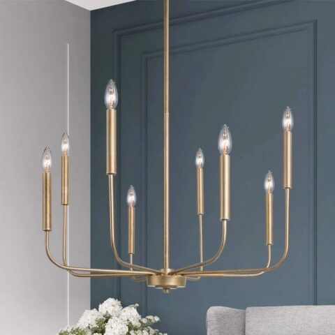 Araña de metal dorado con velas de 8 bombillas. Detrás, al fondo, vemos una pared azul pato, un ramo de flores blancas y un sofá gris claro.