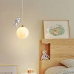 Araña de resina de estilo nórdico con astronauta sobre fondo beige con una cama a la derecha