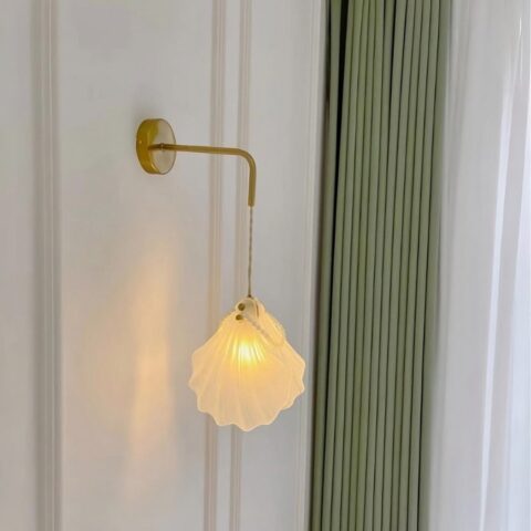 Aplique de cristal y conchas de perla colgado en una pared blanca con una cortina verde al lado.