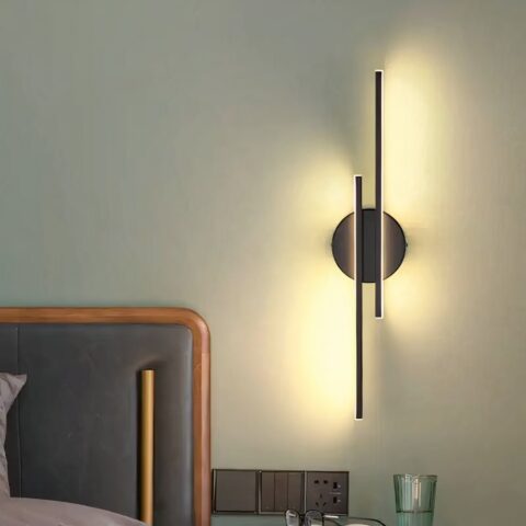Aplique lineal de diseño moderno colgado en la pared de un dormitorio e iluminado, junto a la cama.