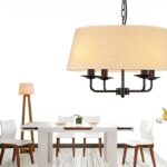 Araña con pantalla de tela beige sobre una mesa de comedor blanca junto a una lámpara de pie