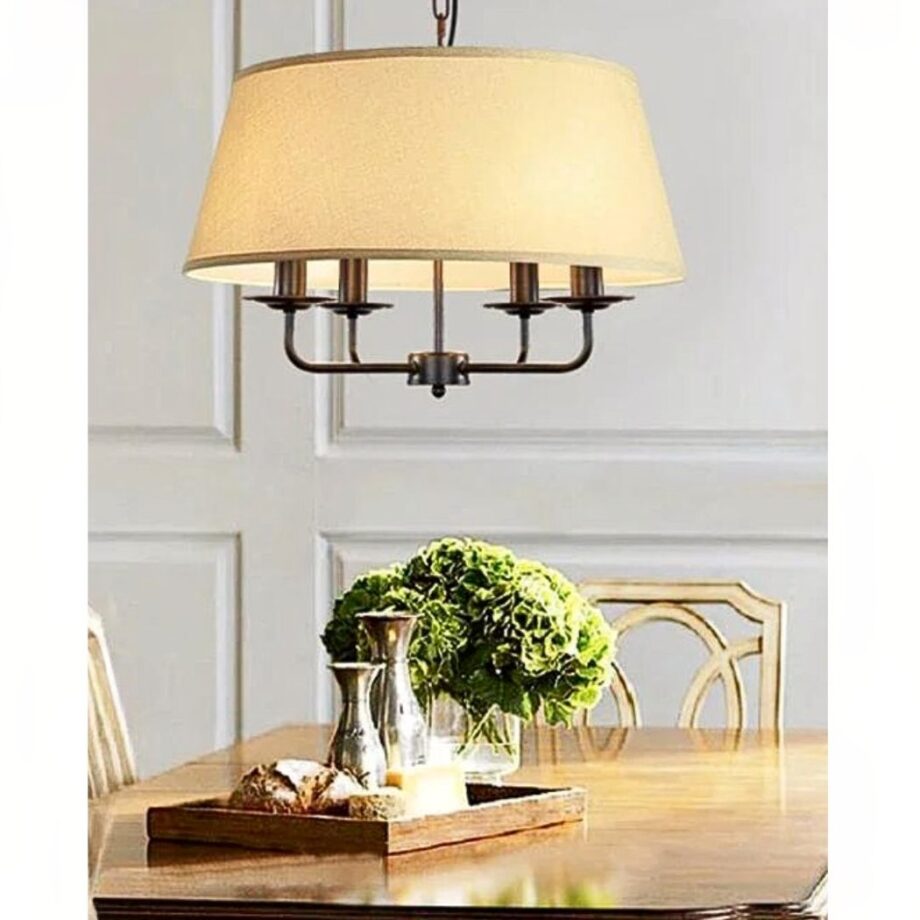 Araña con pantalla de tela beige y cuatro brazos sobre una mesa con centro floral verde