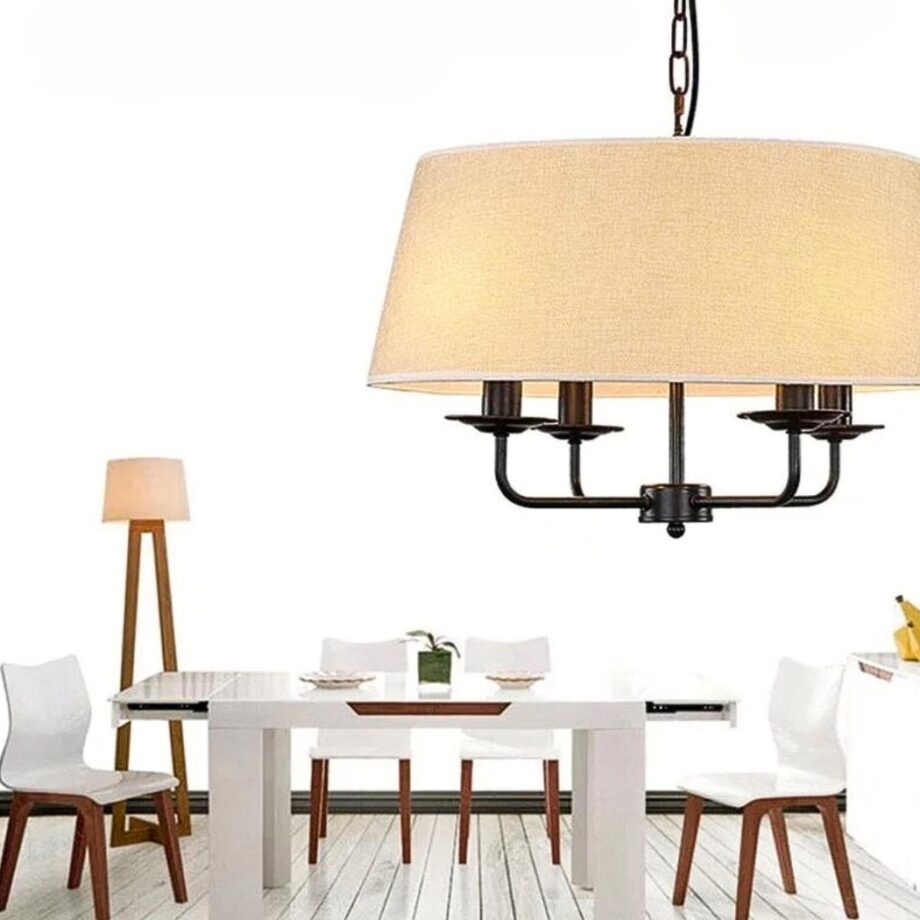 Araña con pantalla de tela beige sobre una mesa de comedor blanca junto a una lámpara de pie