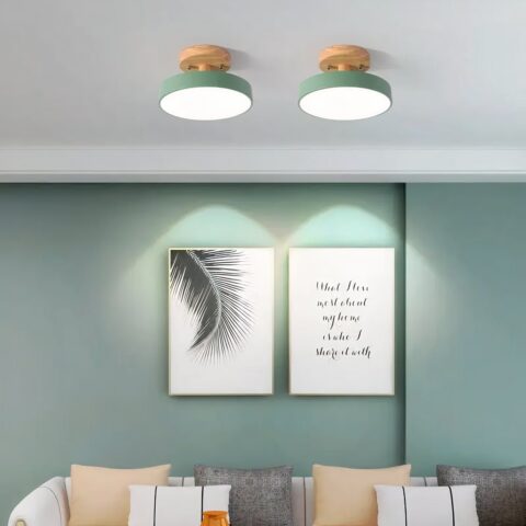 Plafón redondo para dormitorios, en madera y metal, instalado en el techo e iluminado, en la versión verde, encima de un sofá.
