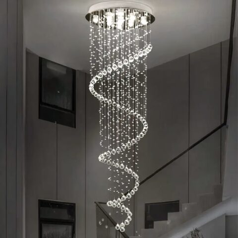 Lámpara de techo en forma de espiral de suspensiones en forma de lágrima. Luz blanca iluminada por varios LED en el soporte redondo plateado fijado al techo. Detrás, una escalera con pasamanos negro y pinturas en la pared.