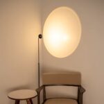 Rincón con lámpara de pie proyectando un óvalo de luz cálida sobre la pared